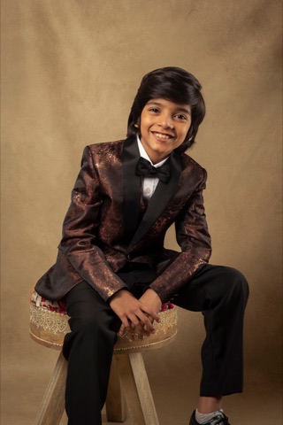 Smiling boy in a patterned suit and bow tie seated on a stool