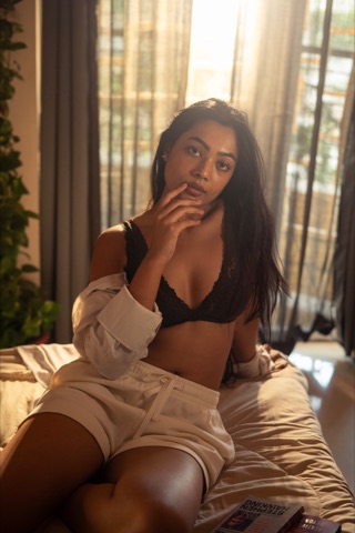 Woman seated on a bed in a black top and white shirt