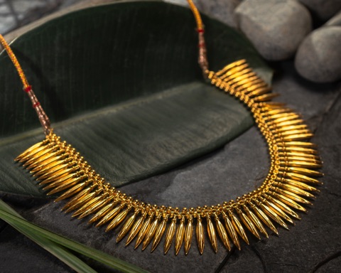 Gold-coloured necklace arranged on dark stones and a leaf