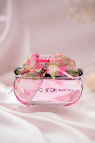 Pink perfume bottle surrounded by flowers and soft fabric