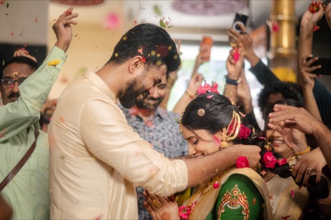 Couple exchanging garlands as guests shower flower petals