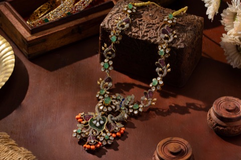 Ornate necklace with green and red stones beside a carved wooden box