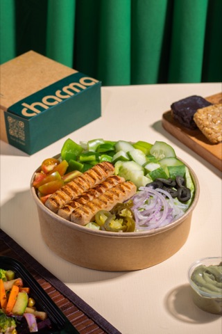 Salad bowl topped with grilled slices beside takeaway packaging
