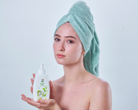 Woman with a towel wrapped around her hair holding a pump bottle