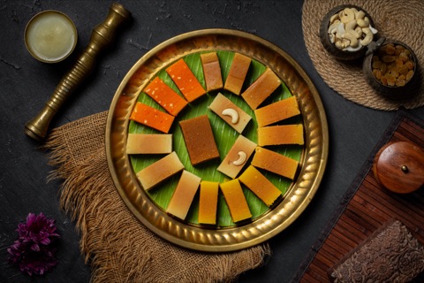 Diamond-shaped sweets arranged on a brass tray with banana leaf