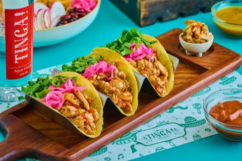 Three tacos topped with pickled onions on a wooden board