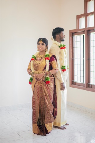 Couple wearing garlands beside a bright window