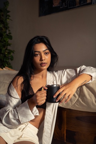Woman in an open white shirt holding a dark mug