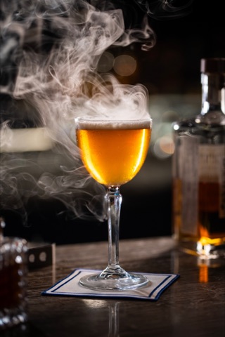 Amber drink in a stemmed glass surrounded by smoke
