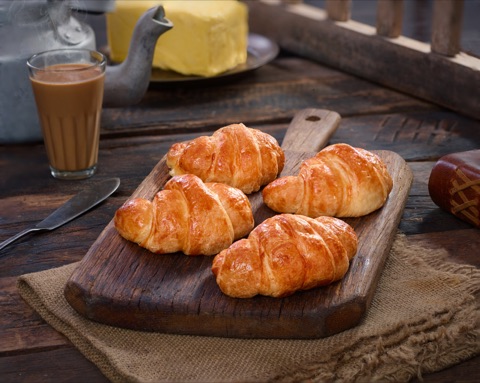 Golden croissants on a wooden board beside tea and butter