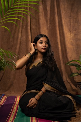 Woman in a black sari seated beside leafy plants