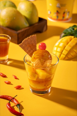 Mango ice cream with a wafer and cherry against a yellow backdrop