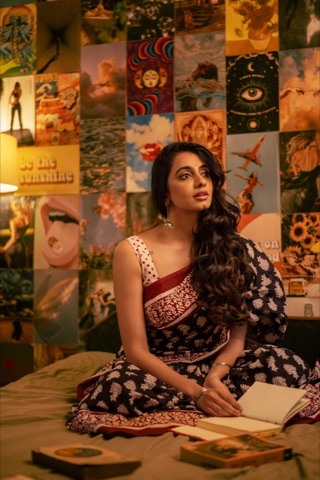 Woman in a patterned sari seated among books and wall posters