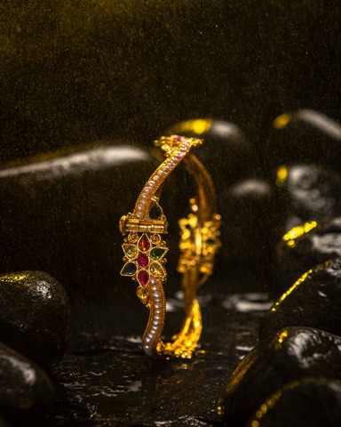 Gold-coloured bracelet with red and green stones on dark rocks