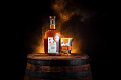 Amber spirits bottle and glass on a wooden barrel