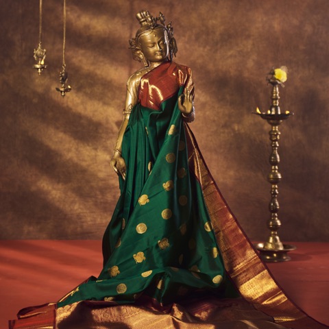 Green and gold sari draped on a sculpted display beside a brass lamp