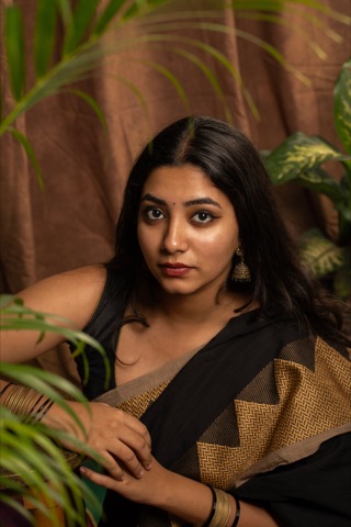Close-up portrait of a woman in a black and gold sari beside plants