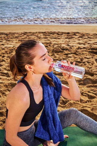 Woman in sportswear drinking from a bottle at the beach