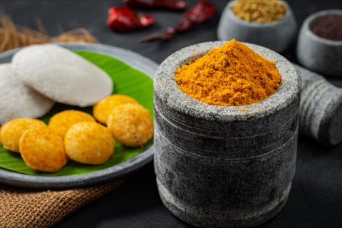 Orange spice powder in a stone mortar beside idli and golden bites