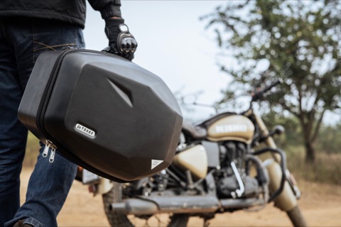Motorcyclist holding a black travel bag beside a motorcycle