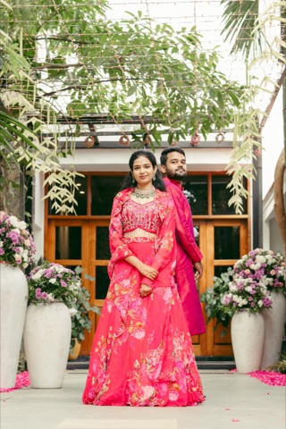Couple in bright pink outfits posing in a flower-filled courtyard