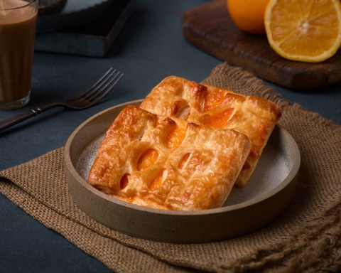 Golden rectangular pastry on a plate beside orange and coffee