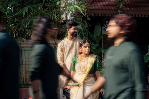 Couple standing in a leafy courtyard as people pass in the foreground