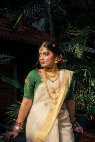 Woman in a cream and green sari seated among foliage