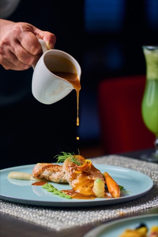 Sauce being poured over a plated restaurant dish