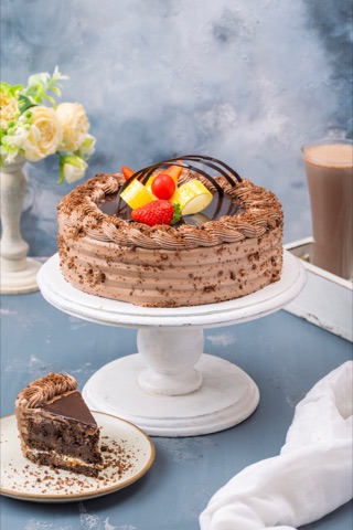 Chocolate layer cake topped with fruit on a white cake stand
