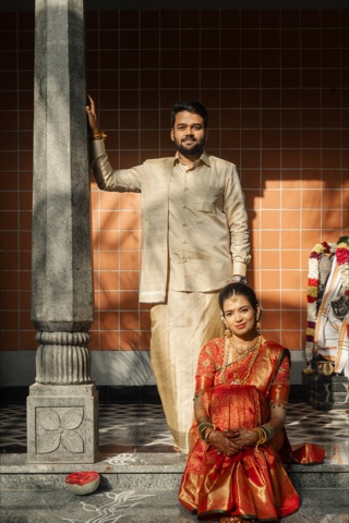 Couple in cream and red wedding attire beside carved stone pillars