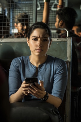 Woman in a blue top holding a phone beside a mirror