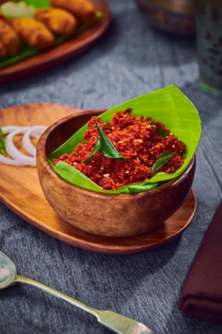 Red spiced dish served in a wooden bowl on banana leaf