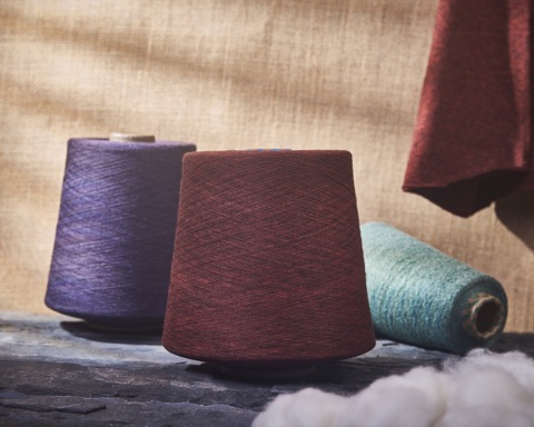 Purple, burgundy and green yarn cones on a fabric surface