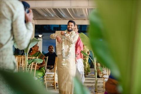Man smiling during a wedding celebration, framed by green leaves