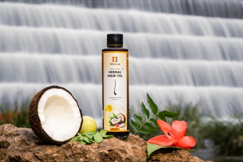 Hair oil bottle with coconut and flowers beside flowing water